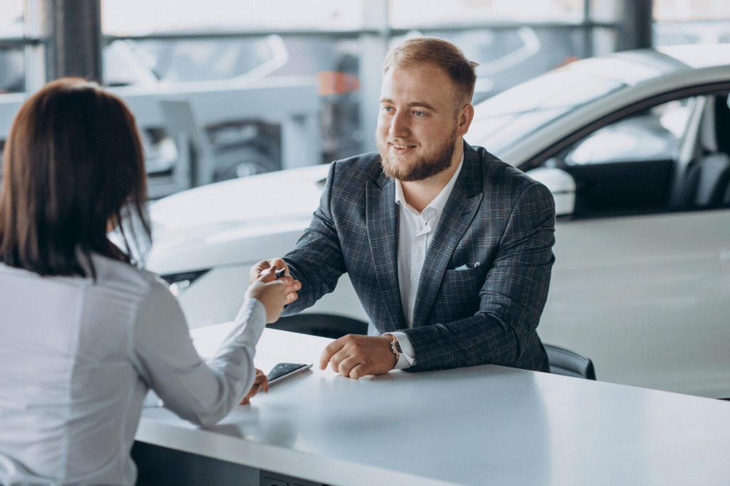 A person in a suit shaking hands with another person at a car dealership.
