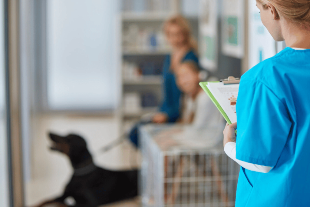 A person in scrubs holding a clipboard in front of a dog.