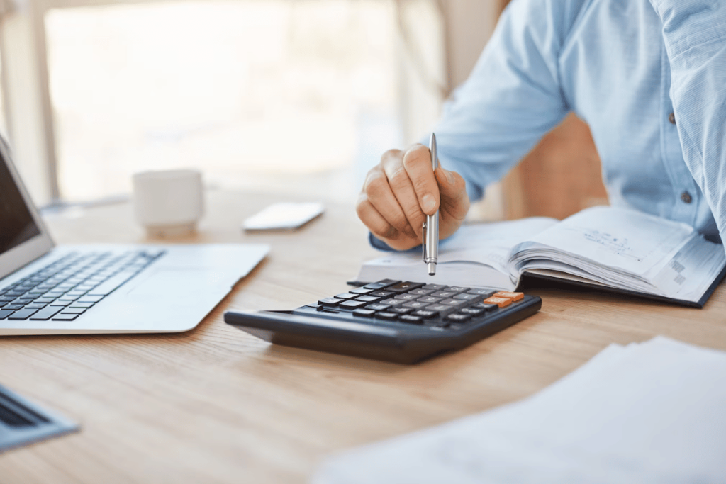 Businessperson in blue shirt performing calculations with a calculator and taking notes.